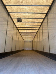 Trailer interior showing long empty cargo space with wooden ceiling panels and metal ribbed walls.