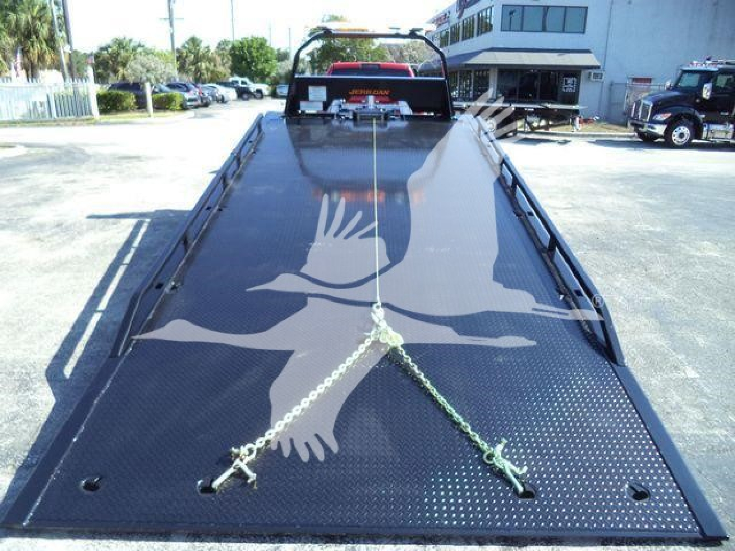 Ram 5500 rollback bed viewed from front, diamond plate steel with two tie-down chains, rear cab visible, dealership lot in background.