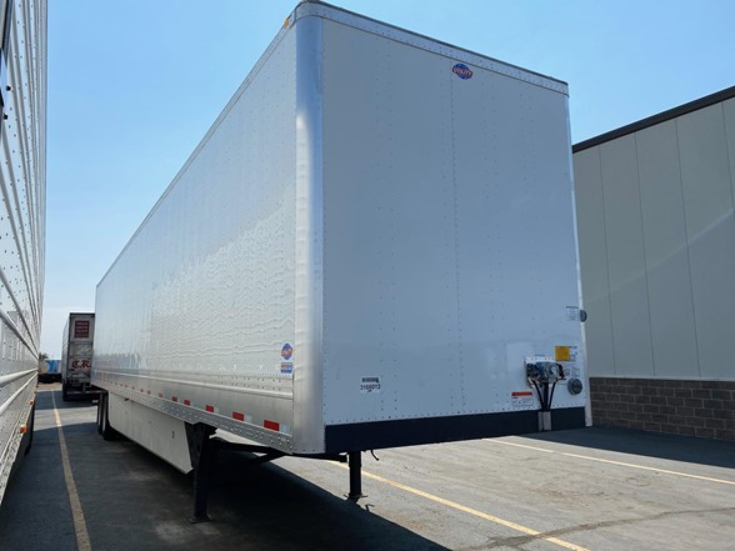 Trailer front-right view of a white Utility 4000DX box trailer in a lot, hitch and support legs visible, with DOT reflectors and branding stickers along the side.