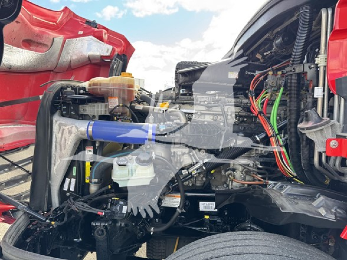 Truck engine bay with exposed components and wiring; hoses, coolant reservoir, and blue silicone hose visible in Freightliner Cascadia engine area.