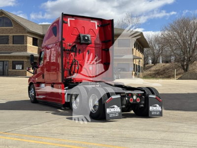 Rear/side view of a red Freightliner Cascadia 126 semi-truck tractor with sleeper cab, dual rear axles, black mudflaps, and parking lot background.