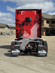 Rear view of a red Freightliner Cascadia 126 tractor with mudflaps and hitch, in a parking lot.