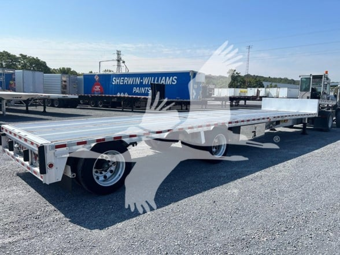 Flatbed trailer showing drop deck configuration with two axles, aluminum deck, and rear lights.