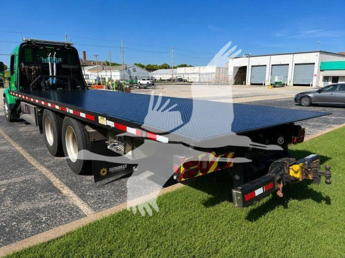 Kenworth T370 rollback truck flatbed trailer with green cab, dual rear axles, and hitch; diamond plate bed with hydraulic controls visible in background.
