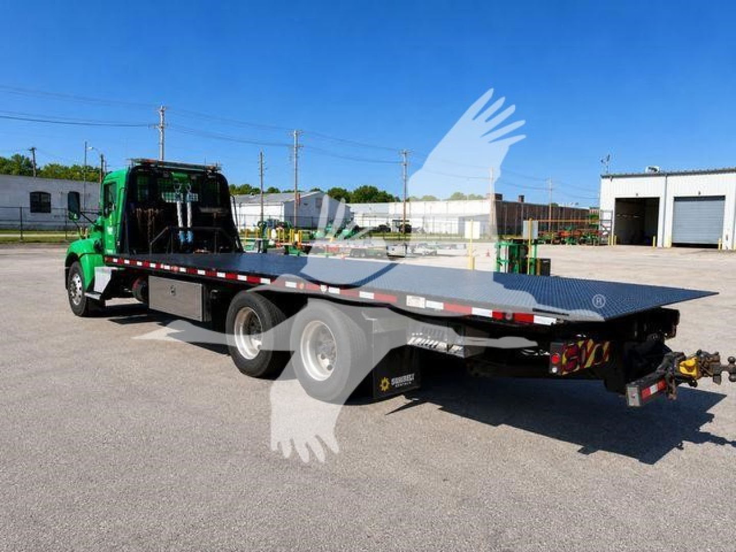 Kenworth T370 rollback tow truck with a green cab and long flatbed, side view showing rear deck and dual rear wheels.