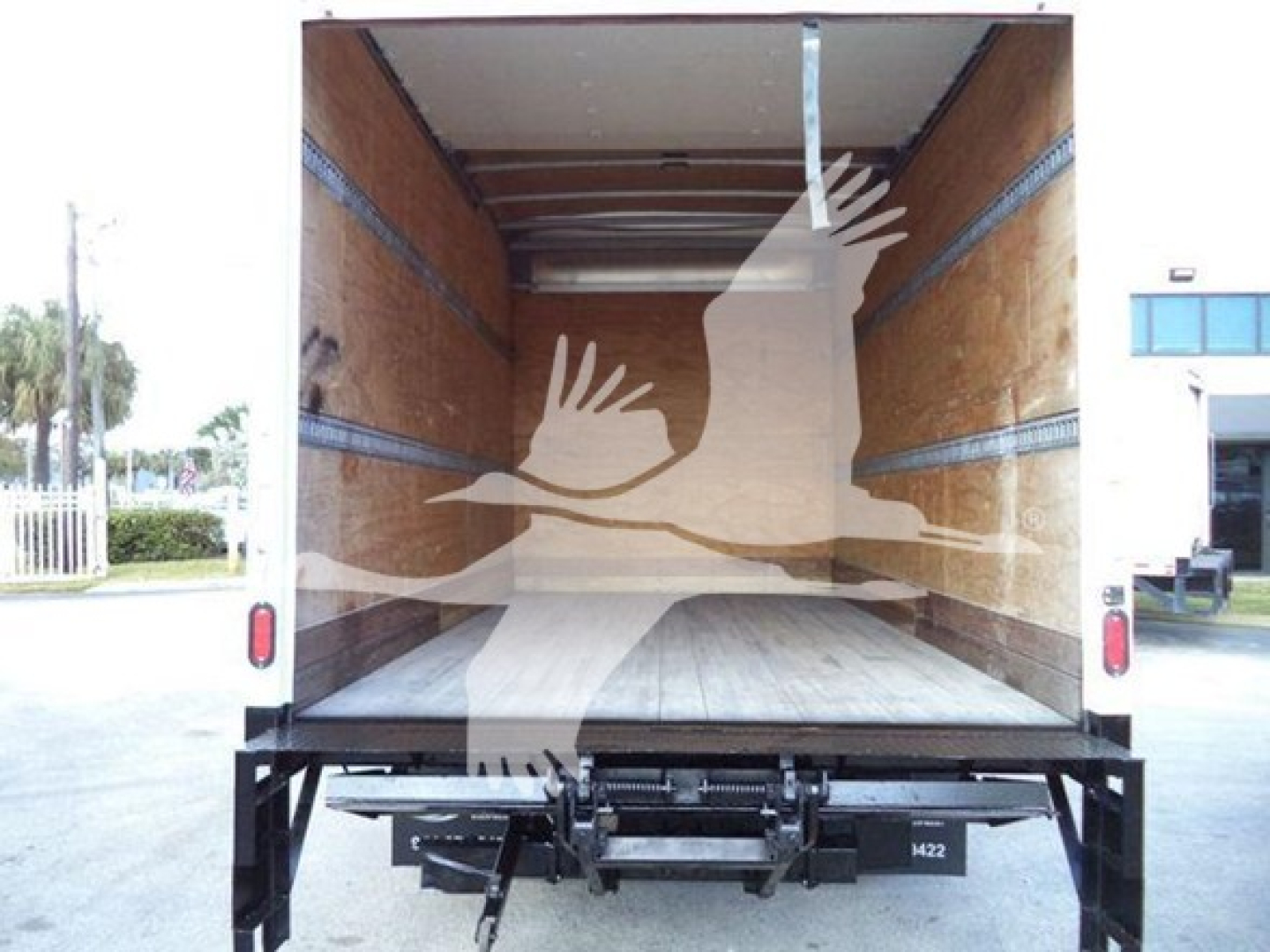 Isuzu NPR-HD box truck cargo area interior showing wooden walls and floor with side rails; rear liftgate lowered.