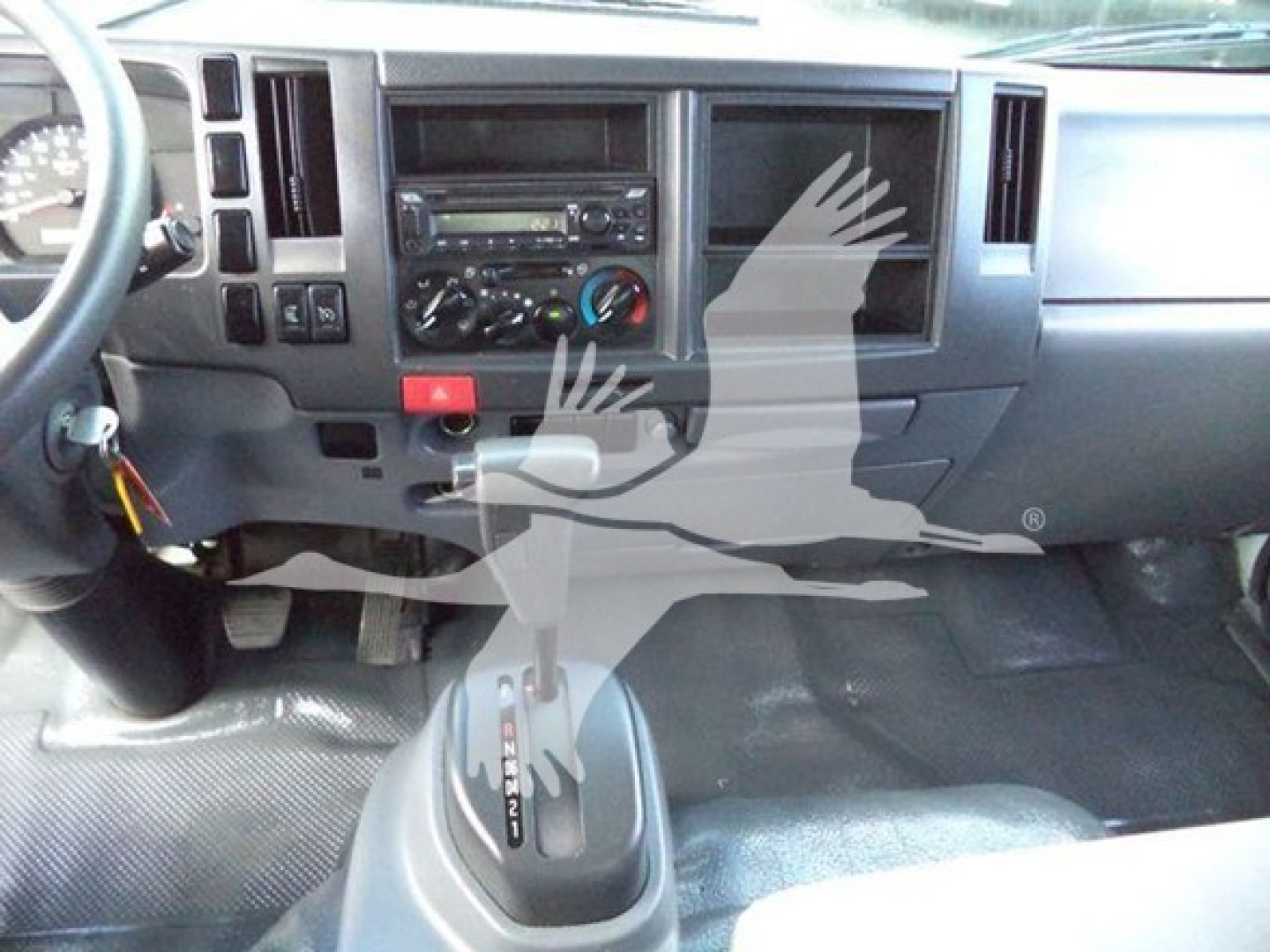 Isuzu NPR HD cab interior with steering wheel, dashboard, radio, climate controls, and gear selector visible.