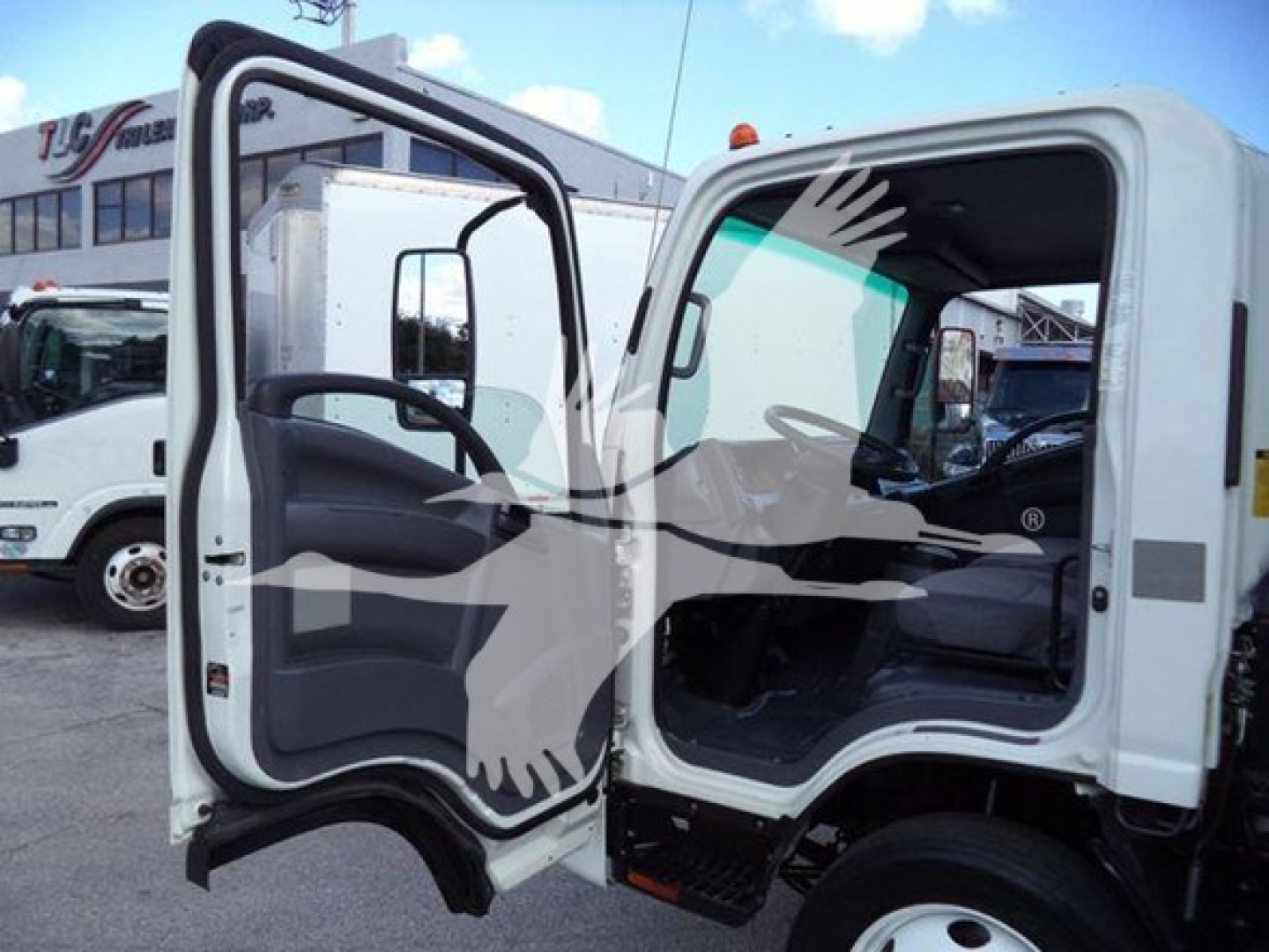 Isuzu NPR HD truck cab open showing interior, with text labeling on dealership lot in background.