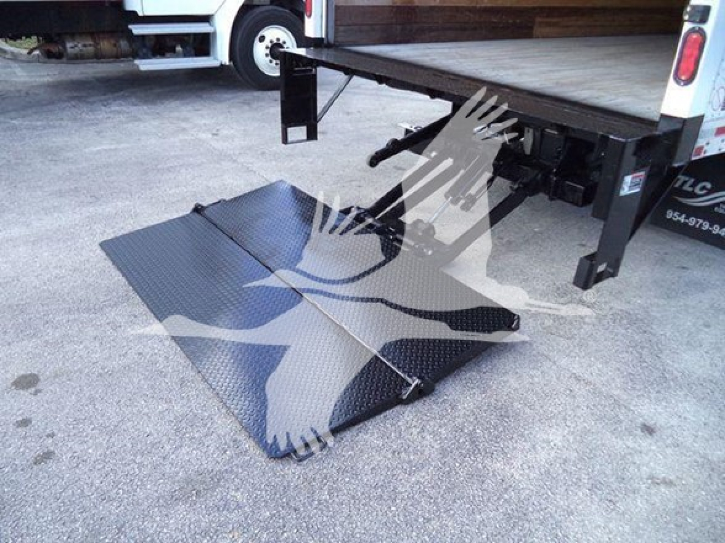 Isuzu NPR HD box truck rear showing fold-out ramp deployed on ground with diamond plate surface and hydraulic lift linkage.