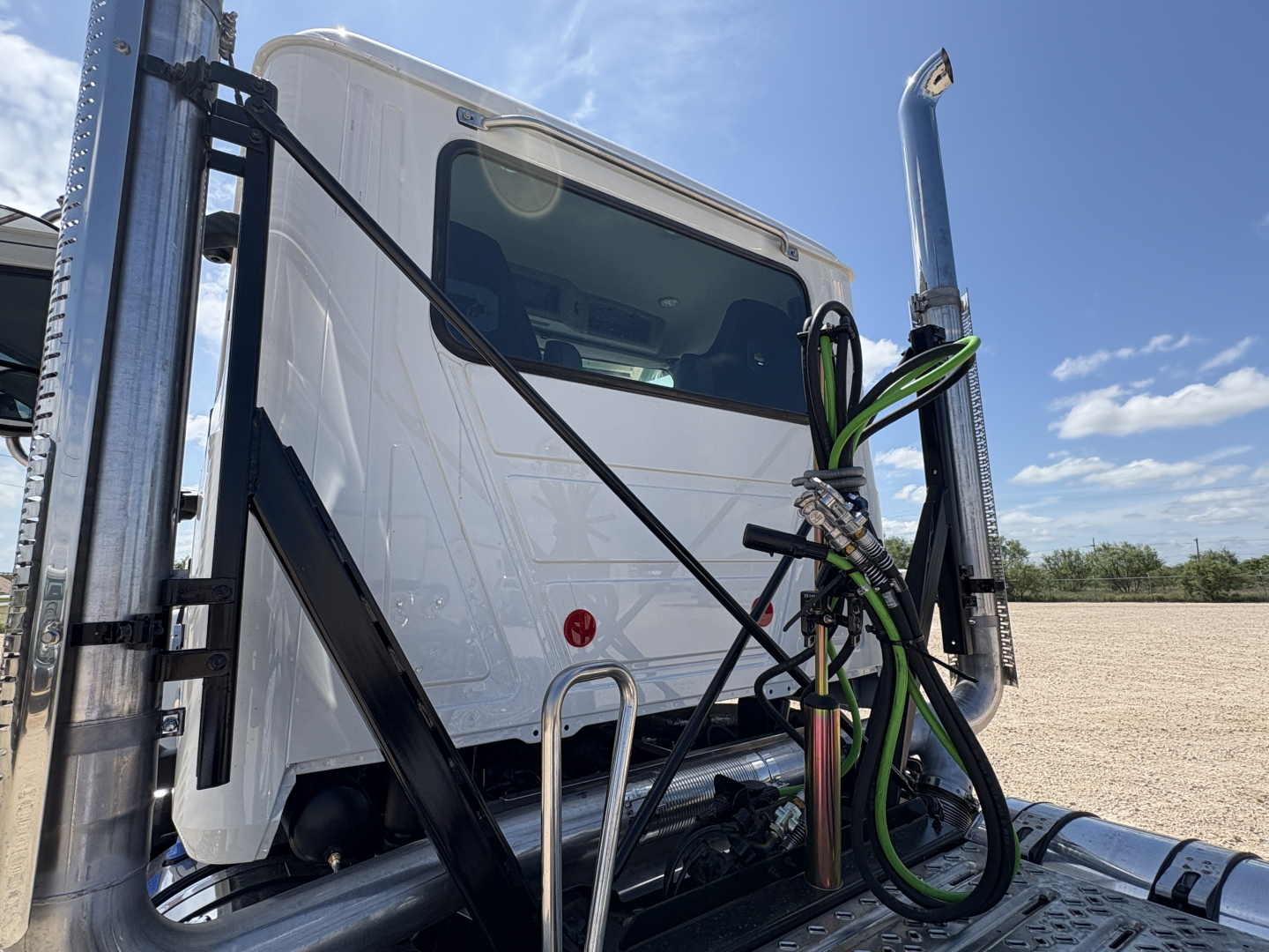 Mack PI64T cab sitting on truck chassis with front window visible; vertical exhaust and fuel lines visible on right; green-and-black hoses attached; daycab configuration.