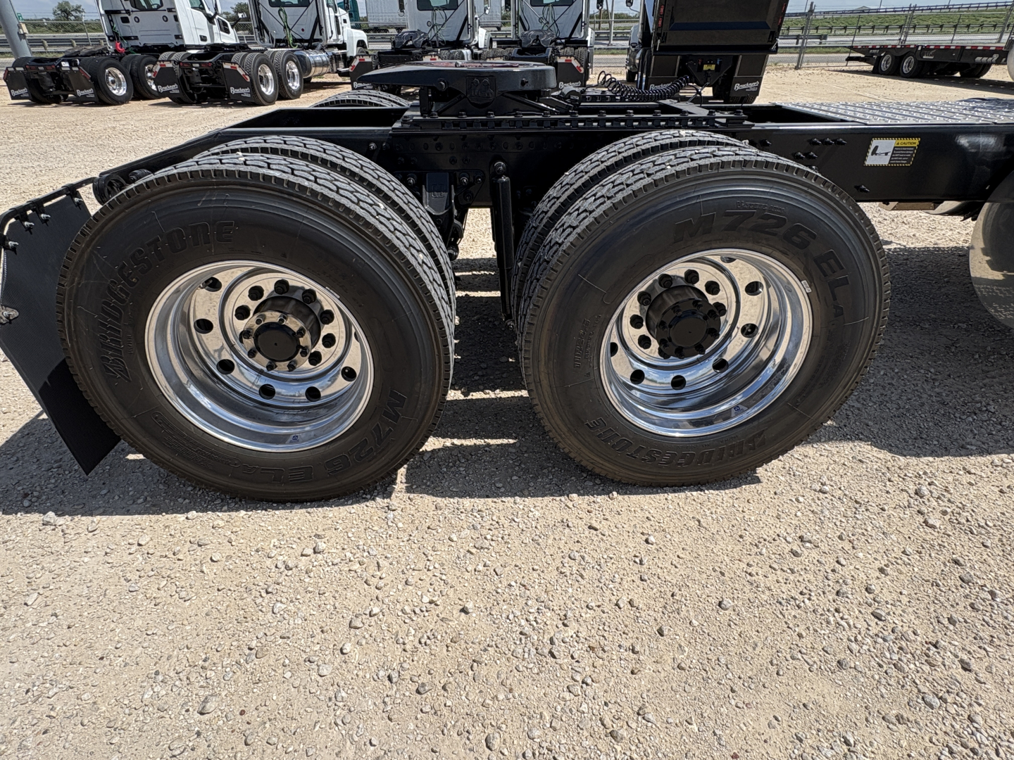Dual rear truck tires on a Mack PI64T chassis showing tire tread, rims, and axle assembly with gravel ground.