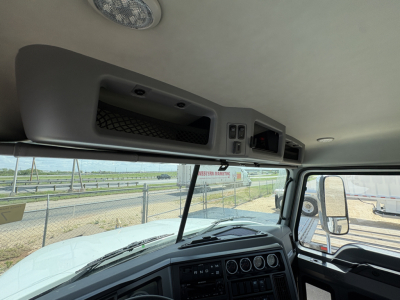 Interior overhead storage and dashboard of a 2027 Mack PI64T truck cab showing overhead console with compartments and control panel, windshield, and dashboard gauges.