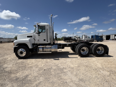 Side view of a white Mack PI64T truck chassis with dual rear axles, flatbed/low-profile frame, chrome exhaust stack, and large front cab.
