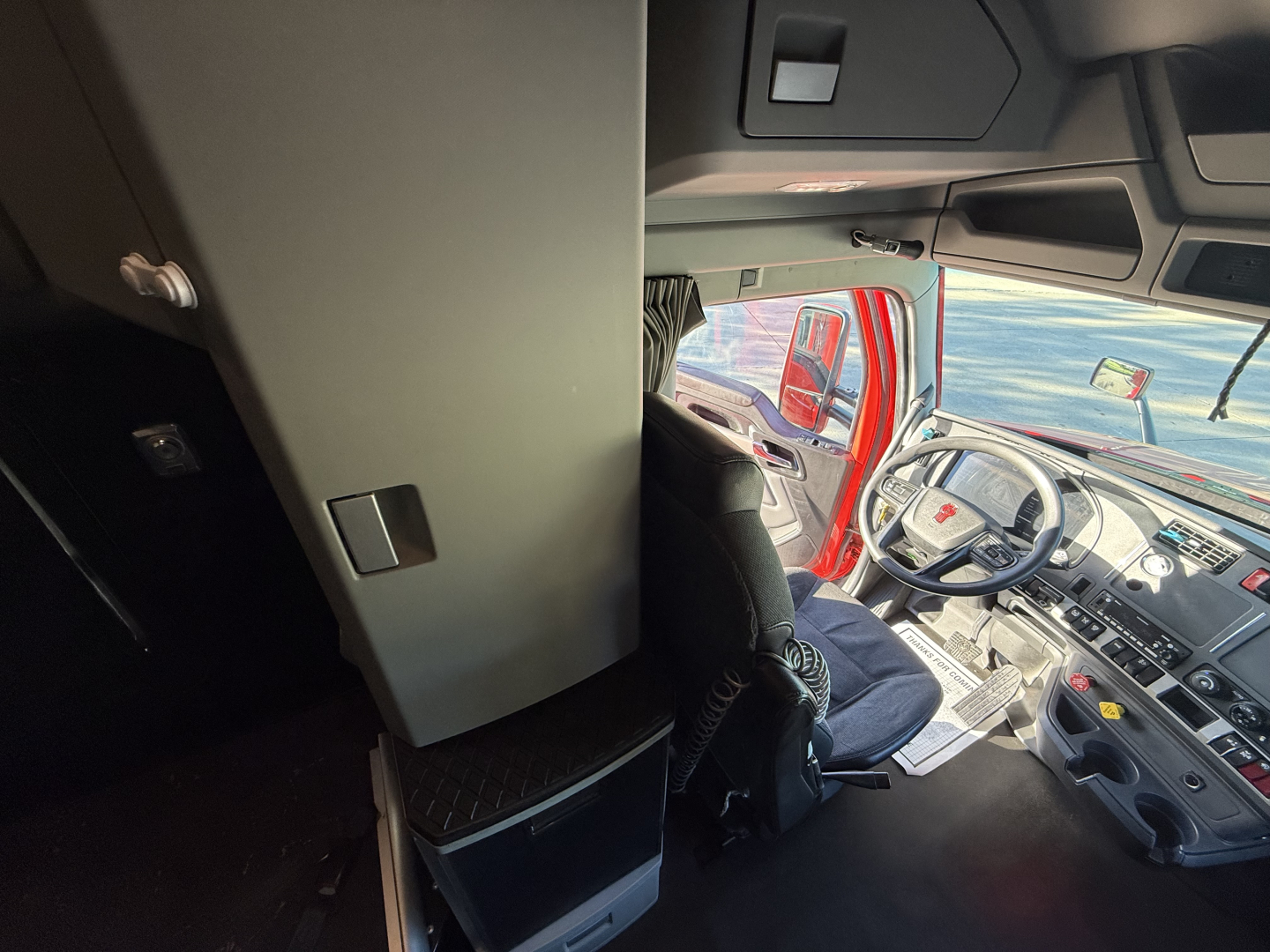 Cab interior of a 2023 Kenworth T680 truck showing dashboard, steering wheel, and driver's seat from a slightly elevated vantage point.