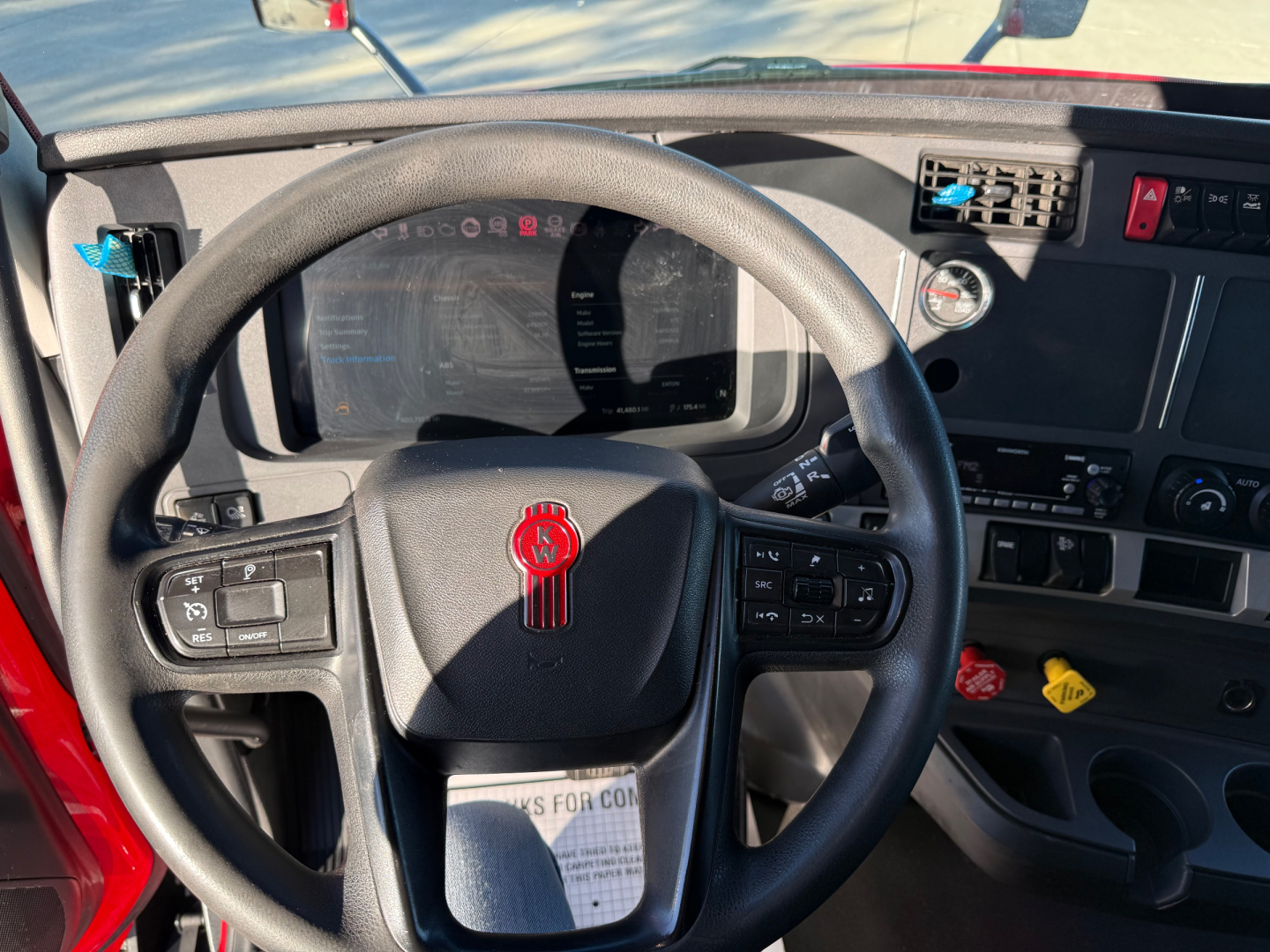 Kenworth T680 cabin view showing steering wheel with red Kenworth badge, dashboard display, instrument cluster, and control panel on the right.