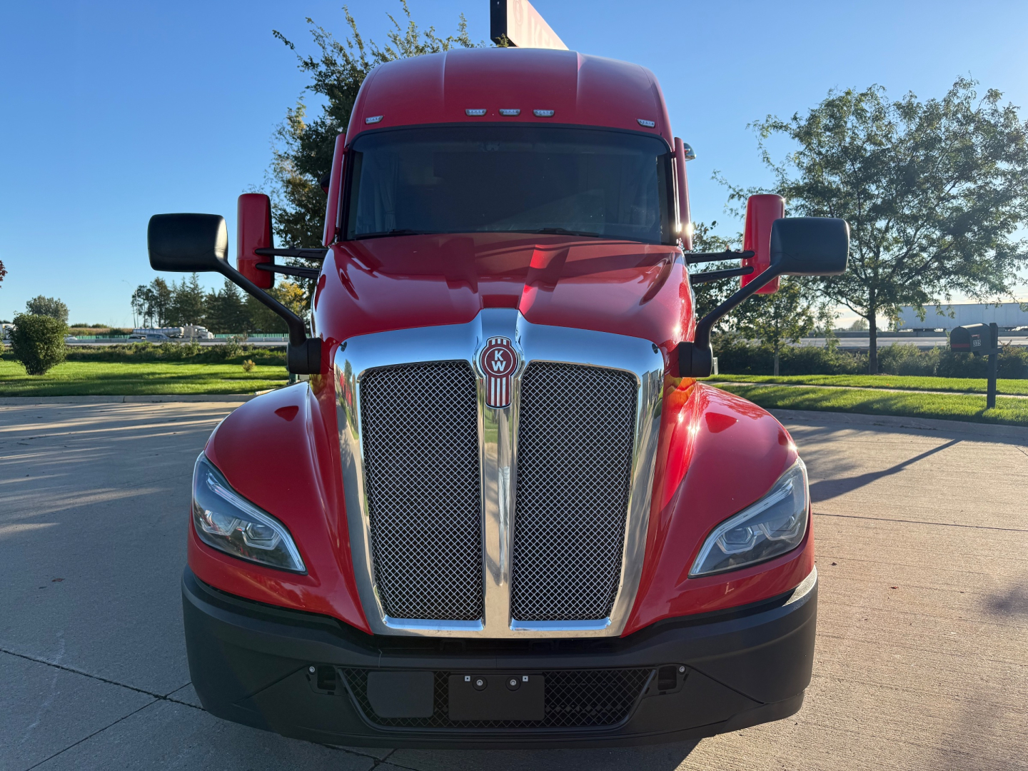 Kenworth T680 front view showing glossy red cab and large chrome grille, stock number 0633358, daytime outdoor setting.
