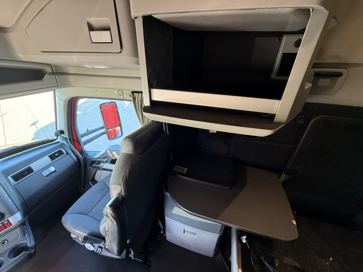 Kenworth T680 truck interior showing overhead storage compartment, fold-out sleeper table, and captain chair with dashboard visible.