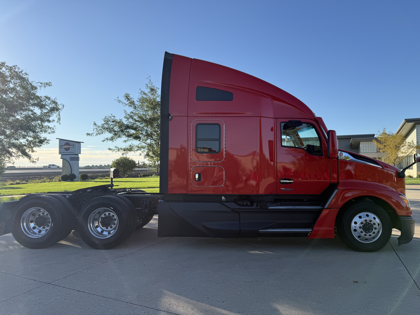 Kenworth T680 tractor in red side view showing sleeper cab with windows and dual rear axles; no visible text on truck side.