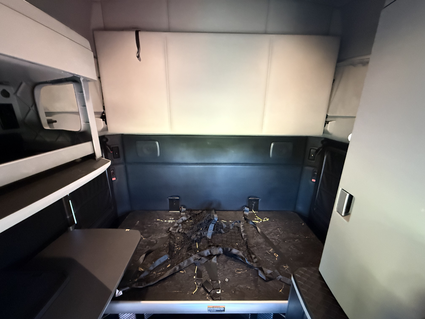Truck interior cargo area of a Kenworth T680 cab with empty bed and some straps on floor; no legible labels visible.