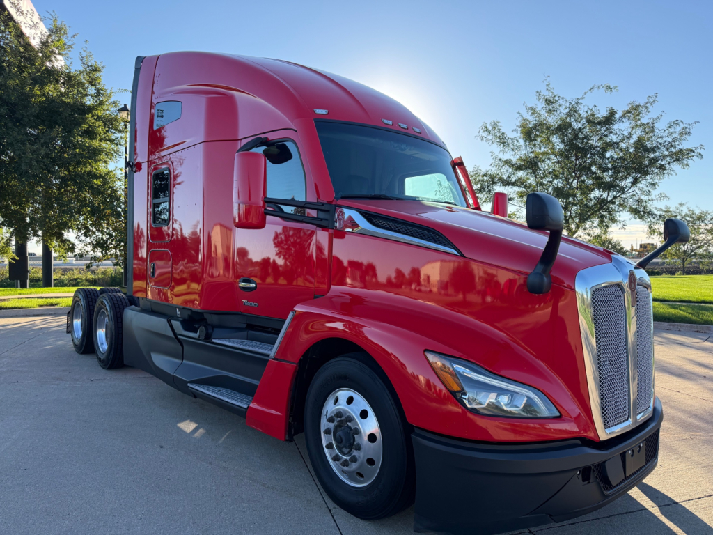 Kenworth T680 sleeper cab truck in red, front three-quarter view showing front grille, headlights, and daytime running lights.