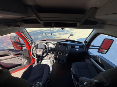 Kenworth truck interior cab front dashboard with steering wheel and seats visible, cabin view from passenger door; no legible labels readable in the image.