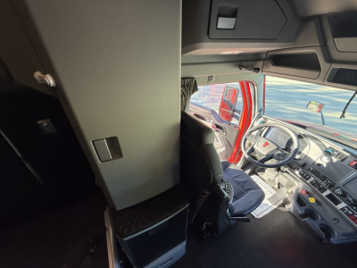 Cab interior of a 2023 Kenworth T680 truck showing dashboard, steering wheel, and driver's seat from a slightly elevated vantage point.