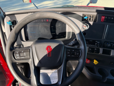Kenworth T680 cabin view showing steering wheel with red Kenworth badge, dashboard display, instrument cluster, and control panel on the right.