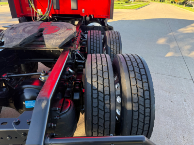 Rear view of a Kenworth tractor chassis showing dual rear wheels, suspension components, and part of the fifth wheel; visible elements include a red frame, black components, and exposed axles.