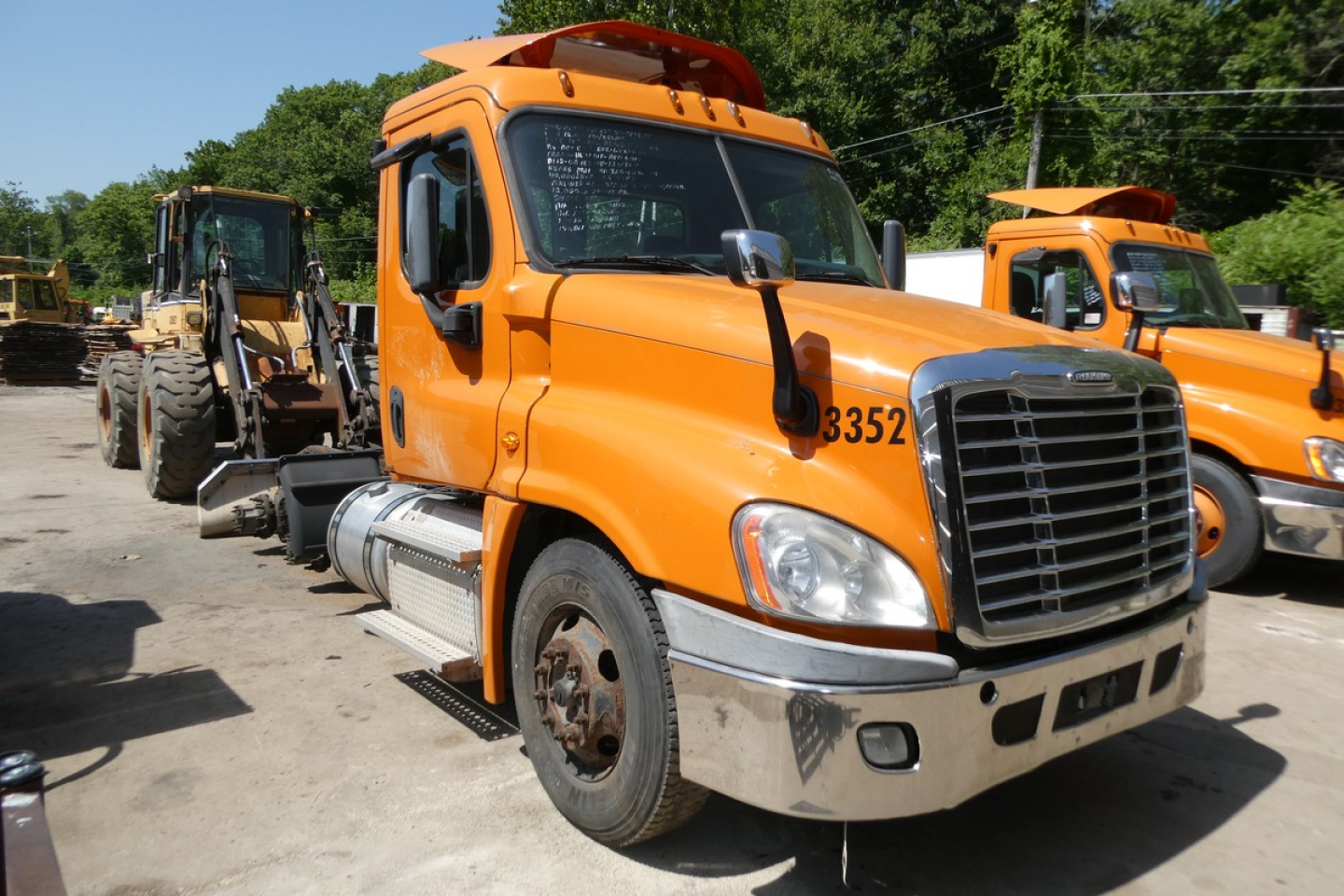 Tractor-trailer truck front cab view showing orange Freightliner Cascadia daycab with large grille, side mirrors, and step rail.