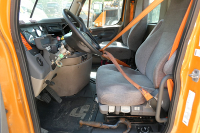 Cab interior of a Freightliner Cascadia 125 daycab showing steering wheel, dashboard, and driver seat with orange seat belt.