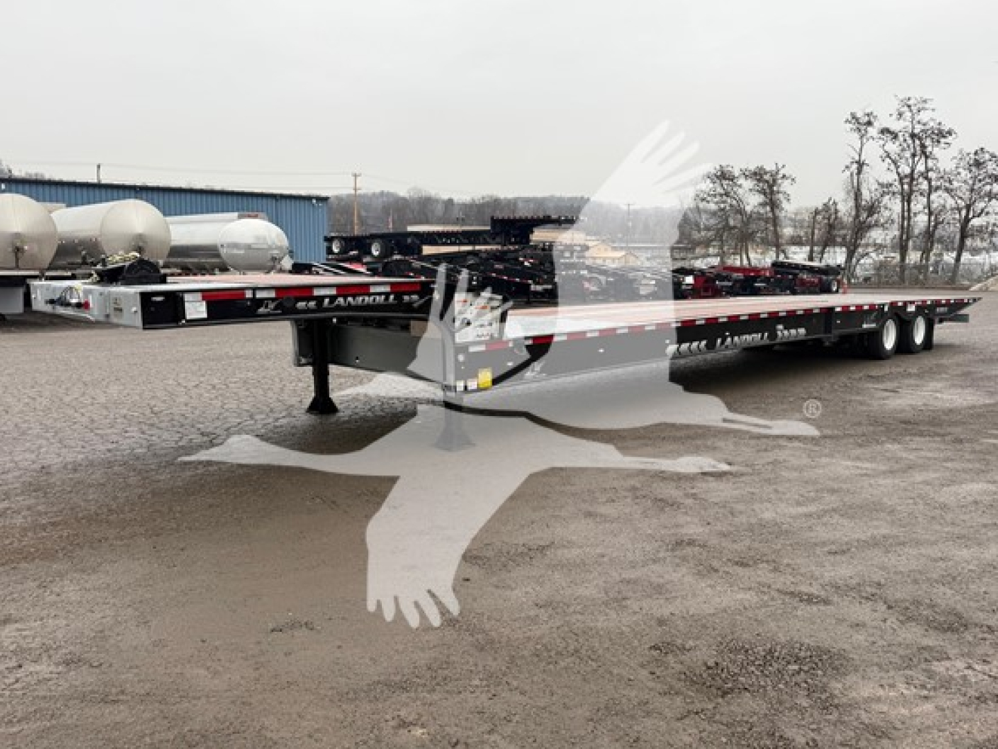 Landoll 930E trailer, low-deck drop deck, long flatbed with dual axles and gooseneck front, Drab black with white logos.