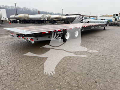 Flatbed trailer showing 930E model on deck with dual rear ramps and triple-axle setup, new Landoll trailer in parking lot.