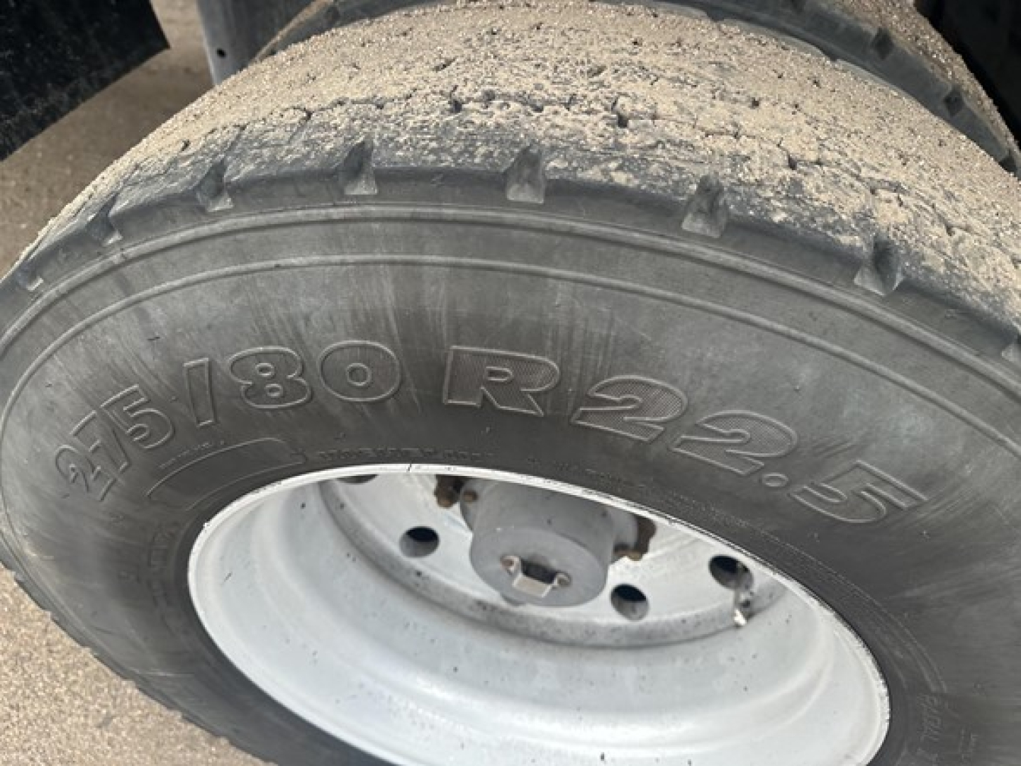 Trailer wheel showing 225/80R22.5 tire with rim and dirt on tread beside mudguard.