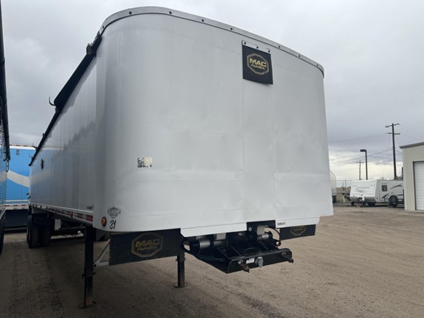 Frameless aluminum end dump trailer in a yard, rear view showing MAC logo, hitch, and support legs.