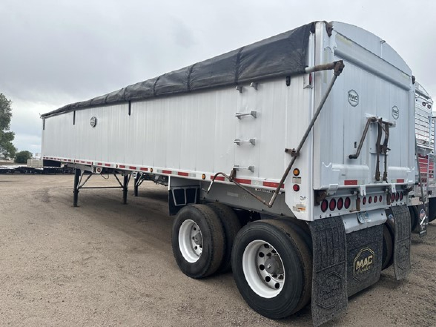 Mac MVP frameless aluminum end dump trailer with tarped top, dual rear wheels, and MAC logo on mudflaps.