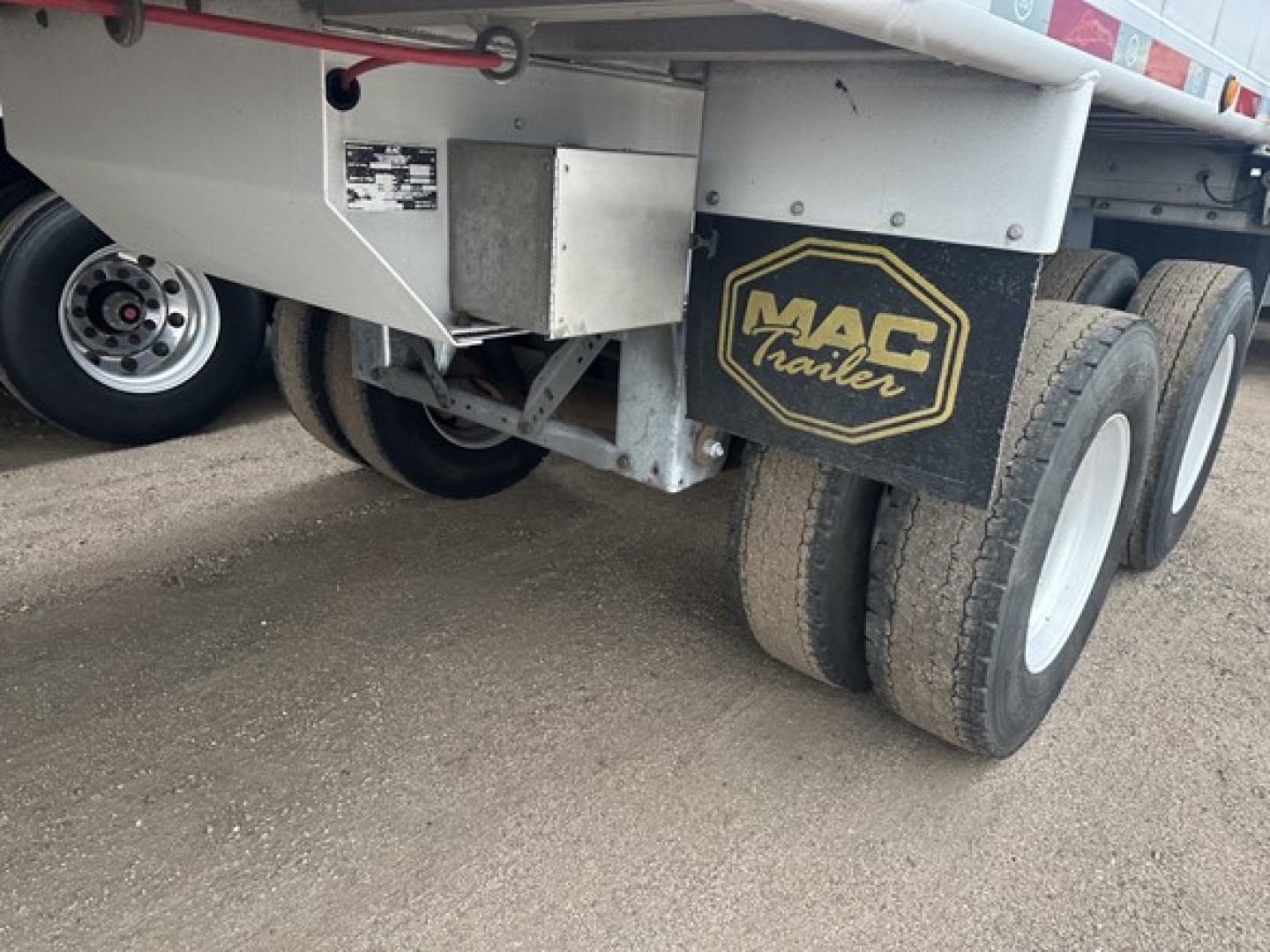 Mac Trailers frameless aluminum end dump undercarriage showing dual rear axles and MAC Trailers mudflap, with VIN plate and stock label near the side.
