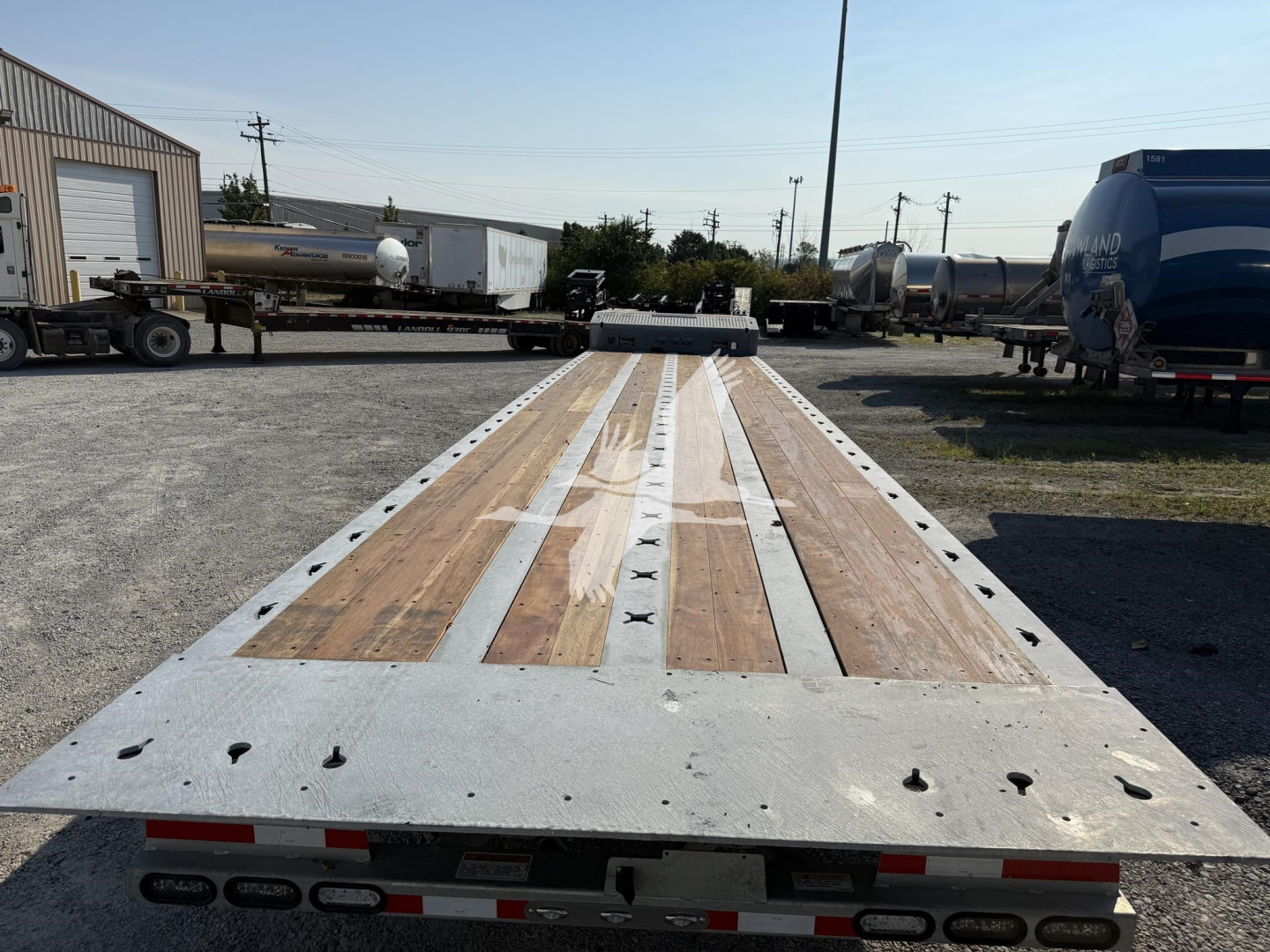 Flatbed trailer deck with wooden planks and metal frame showing numerous tie-down slots; visible in a trailer yard.