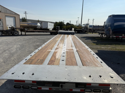 Flatbed trailer deck with wooden planks and metal frame showing numerous tie-down slots; visible in a trailer yard.