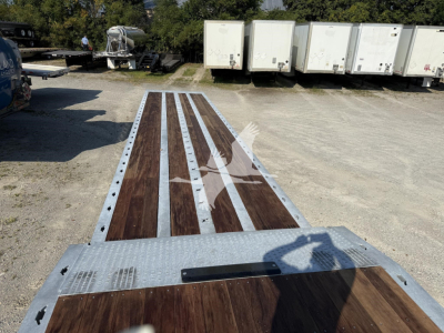 Landoll 440 trailer deck showing wooden planks with metal edge rails and perforated silver sills; long trailer frame in a yard with other trailers in background.