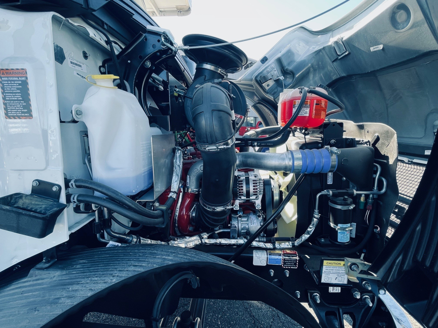 Engine bay of a 2026 Mack MD6 showing coolant reservoir, hoses, belts, and intercooler piping with various labels.