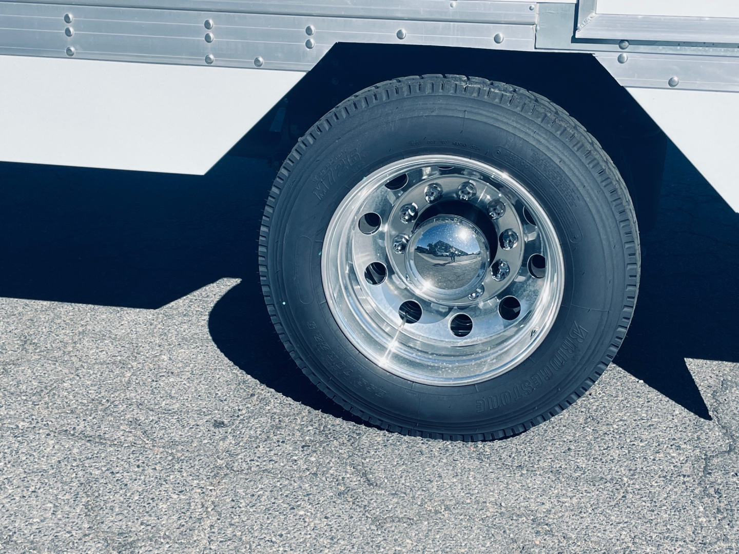 Truck wheel and side of box trailer showing chrome wheel, tire, and riveted aluminum body.