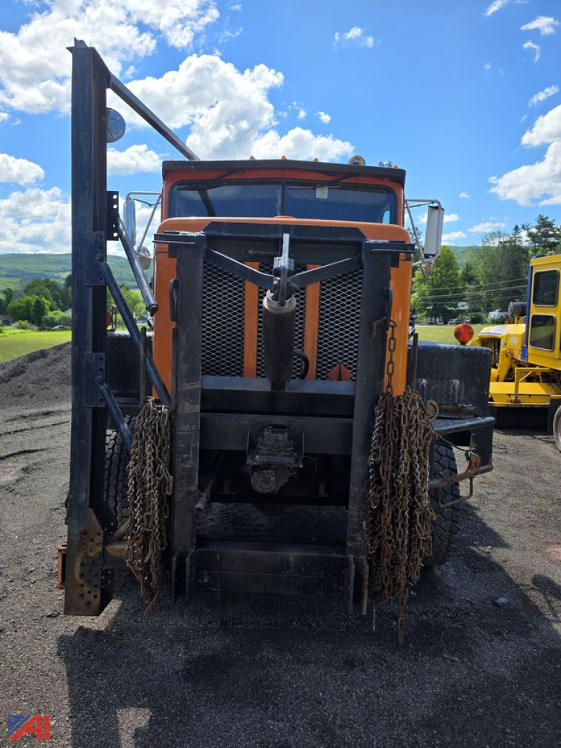 Front view of an orange International dump truck with a tall grille, chains hanging from both sides, and a winch in the center. Blue sky with clouds in the background.
