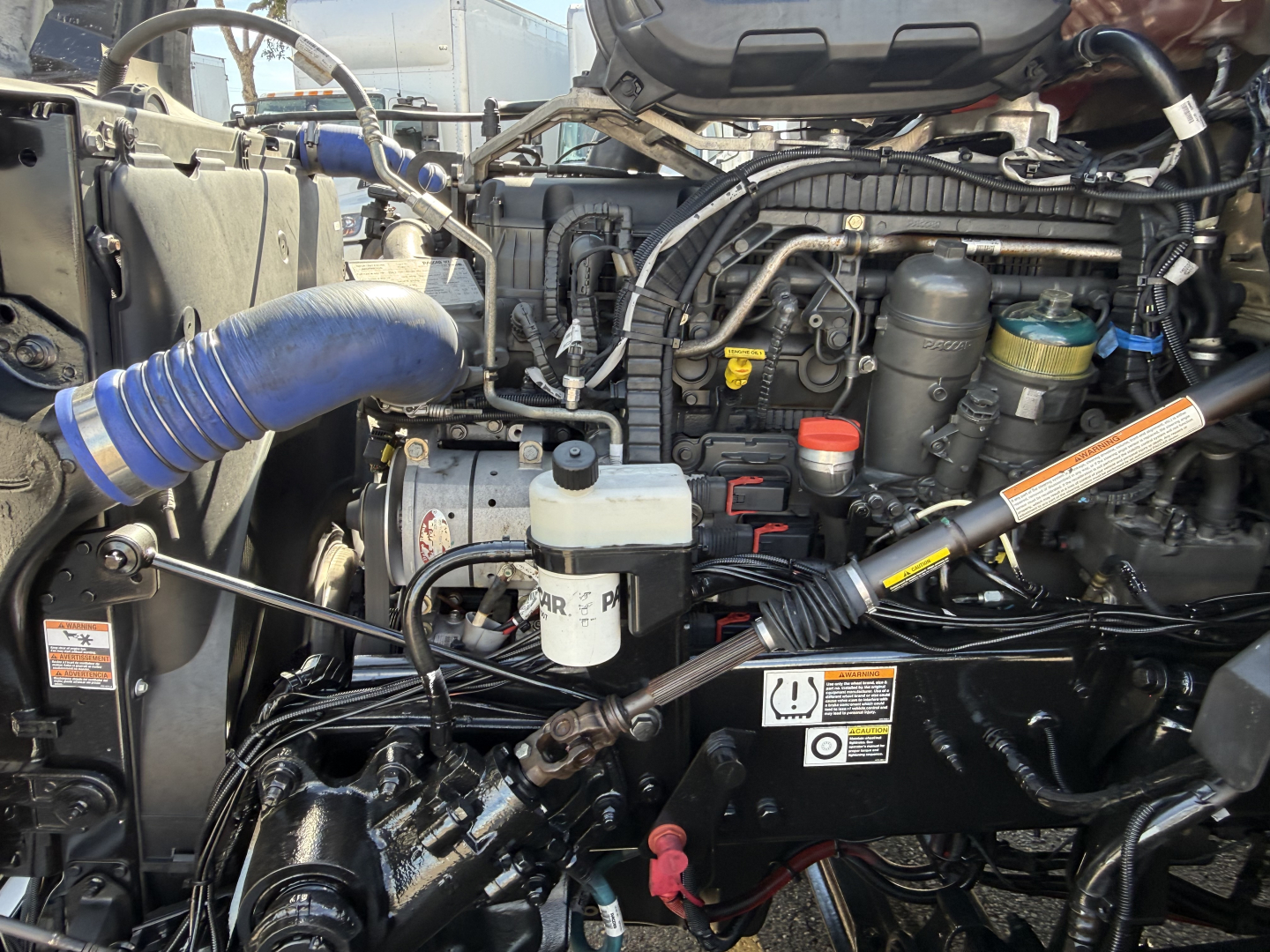 Kenworth T680 engine bay showing coolant reservoir, assorted hoses, and engine components.