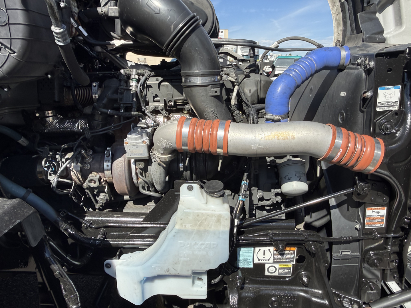 Kenworth T680 engine bay view showing air intake tubing, coolant reservoir, hoses, and turbocharger components.
