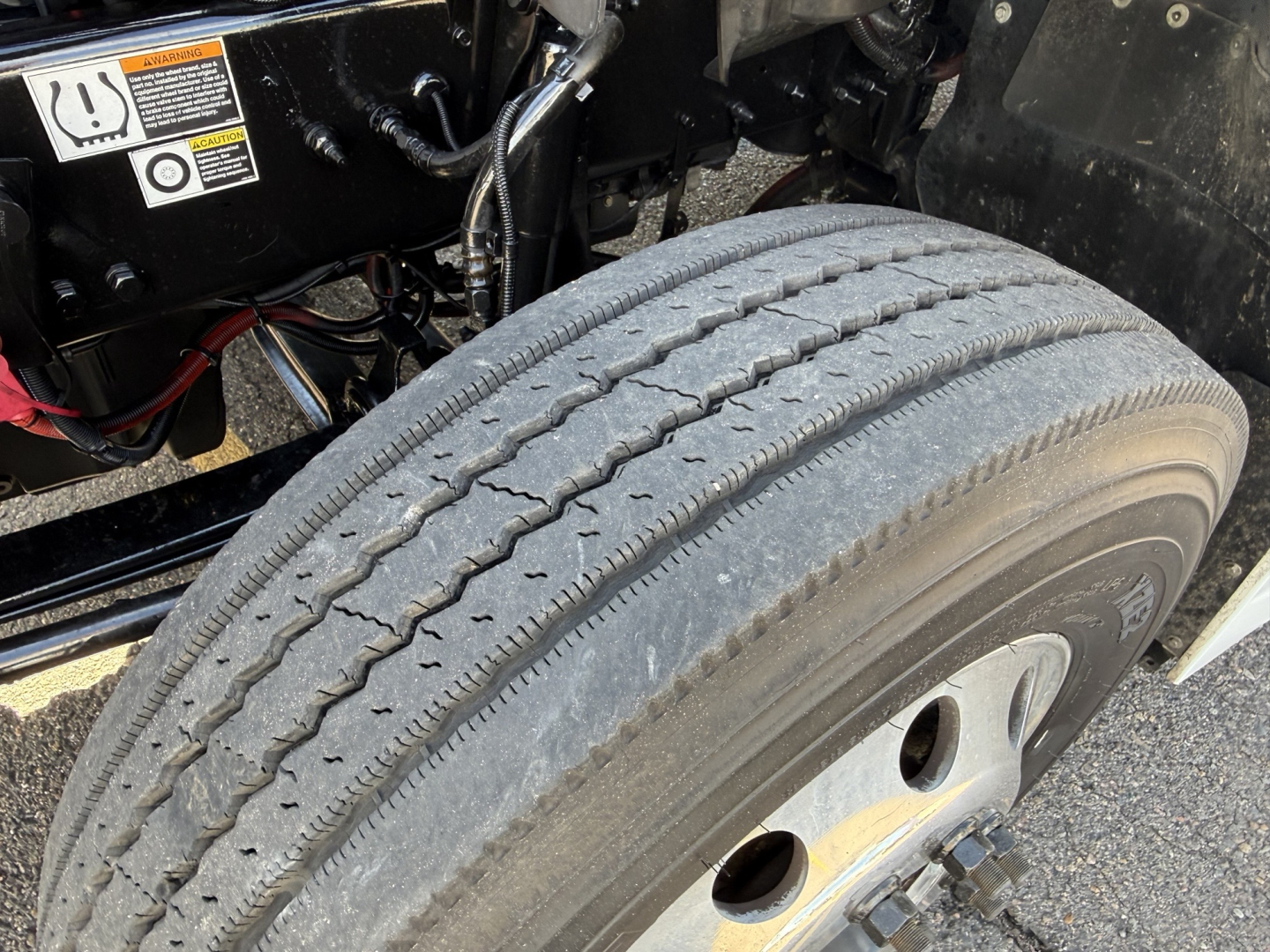 Kenworth T680 truck front tire and wheel well showing dual rear highway tire and suspension components.
