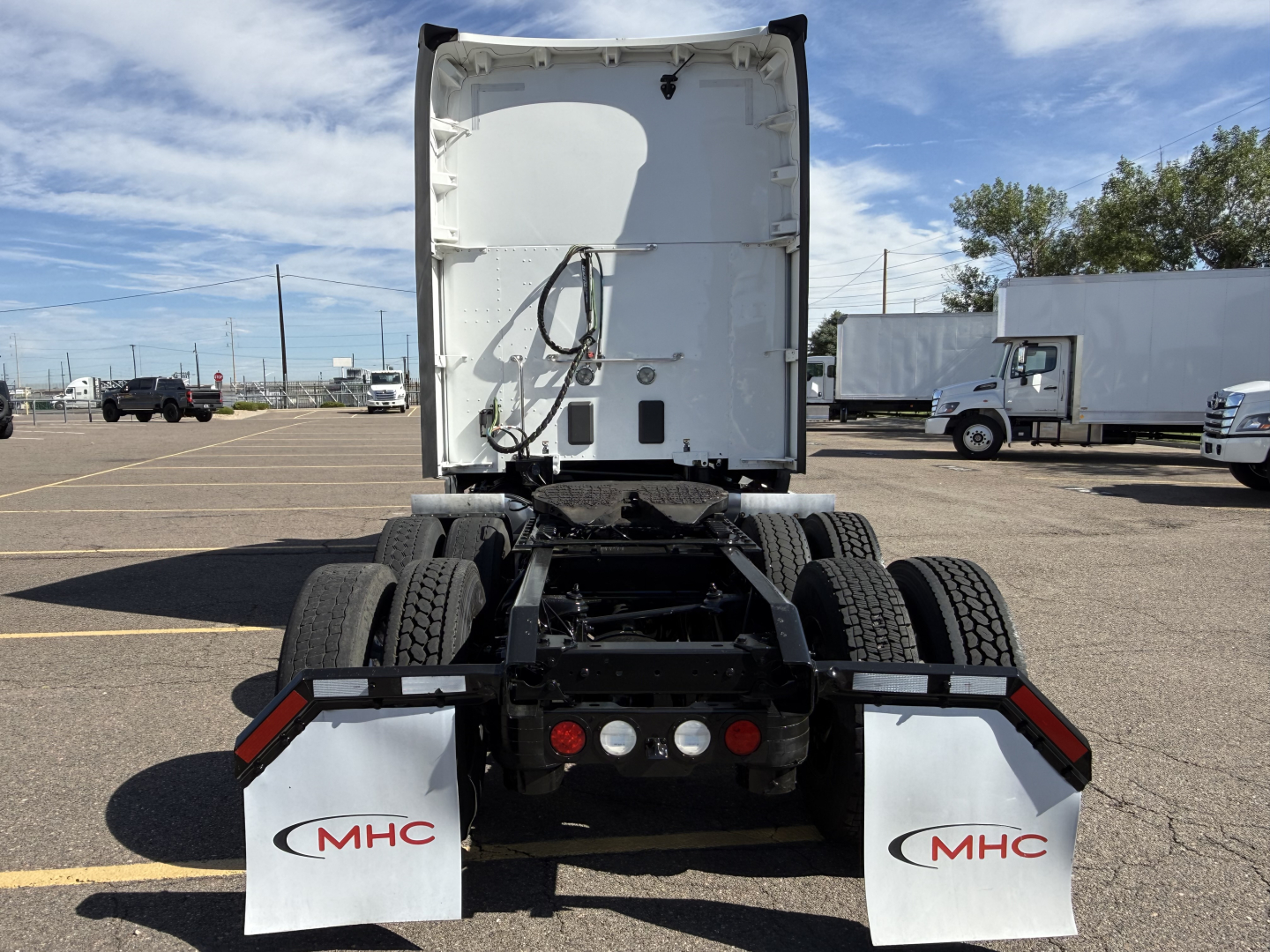 Kenworth T680 semi-truck tractor rear view showing triple-axle chassis, mud flaps with MHC logo, lights, and white sleeper cab door at the back.