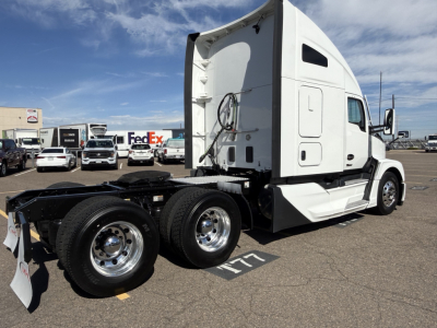 Kenworth T680 conventional sleeper truck in a parking lot, side view highlighting rear tandem axles and white cab with sleeper pod.