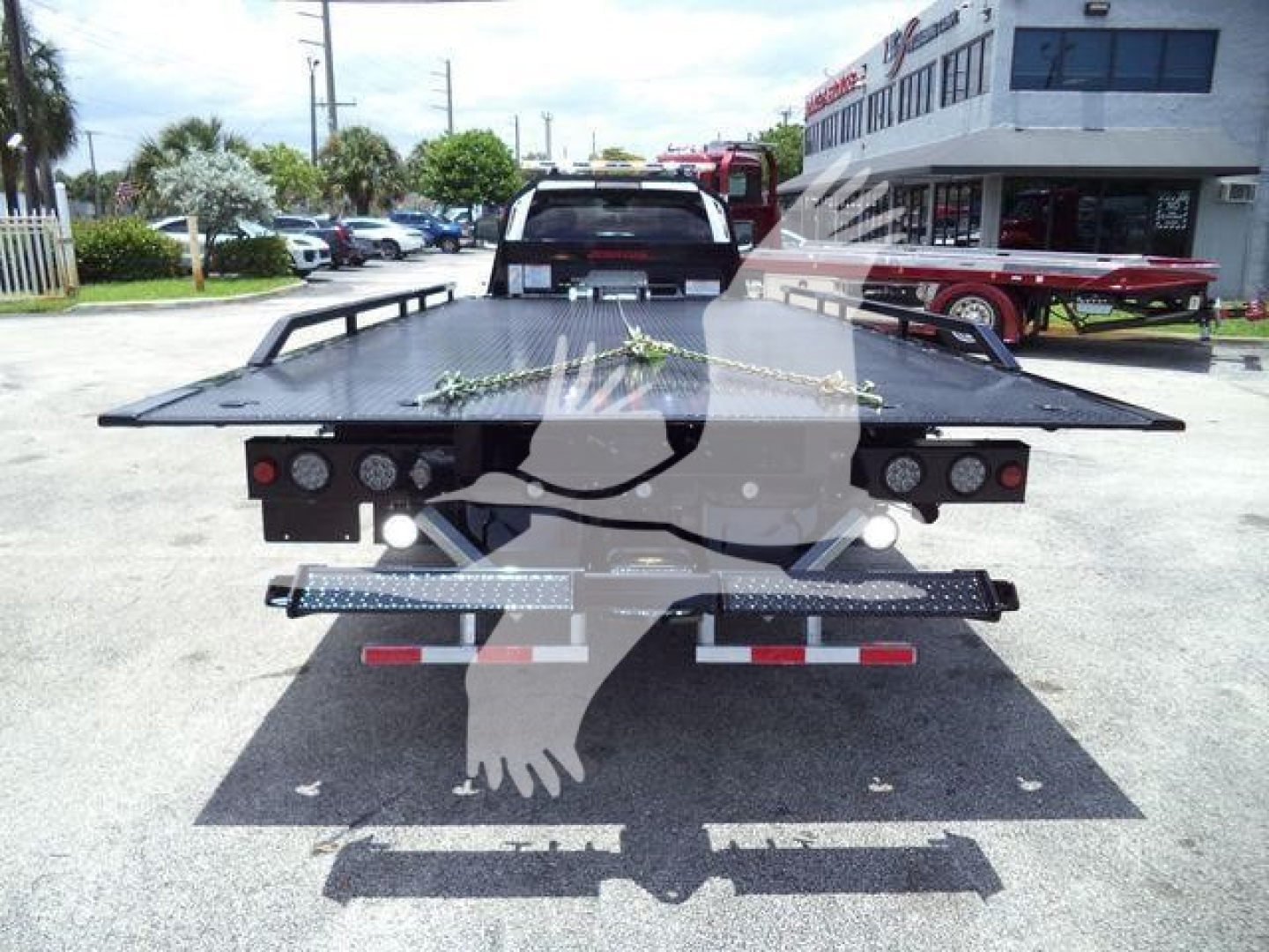 Ram 5500 rollback flatbed truck seen from rear with chains and lights on the bed, dealership lot in background.