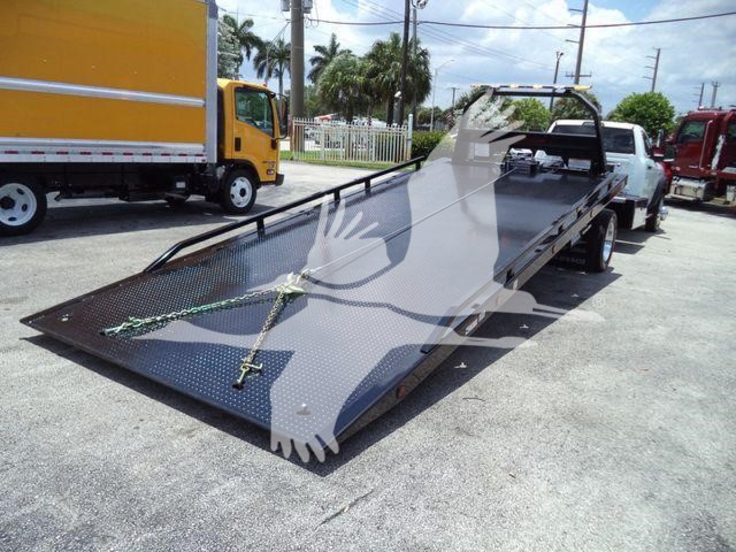 Flatbed tow truck trailer attached to a Ram 5500 SLT, loading platform with ramps and safety chains visible.