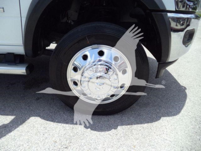 Front wheel and tire of a white Ram 5500 SLT truck showing chrome hubcap, wheel well, and fender; partial grille and bumper visible.